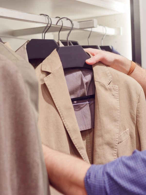 Young man choosing suit jacket during apparel shopping at clothing store